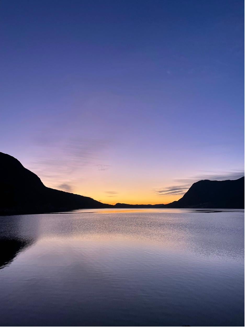 Speilblank fjord i solnedgang med fjell