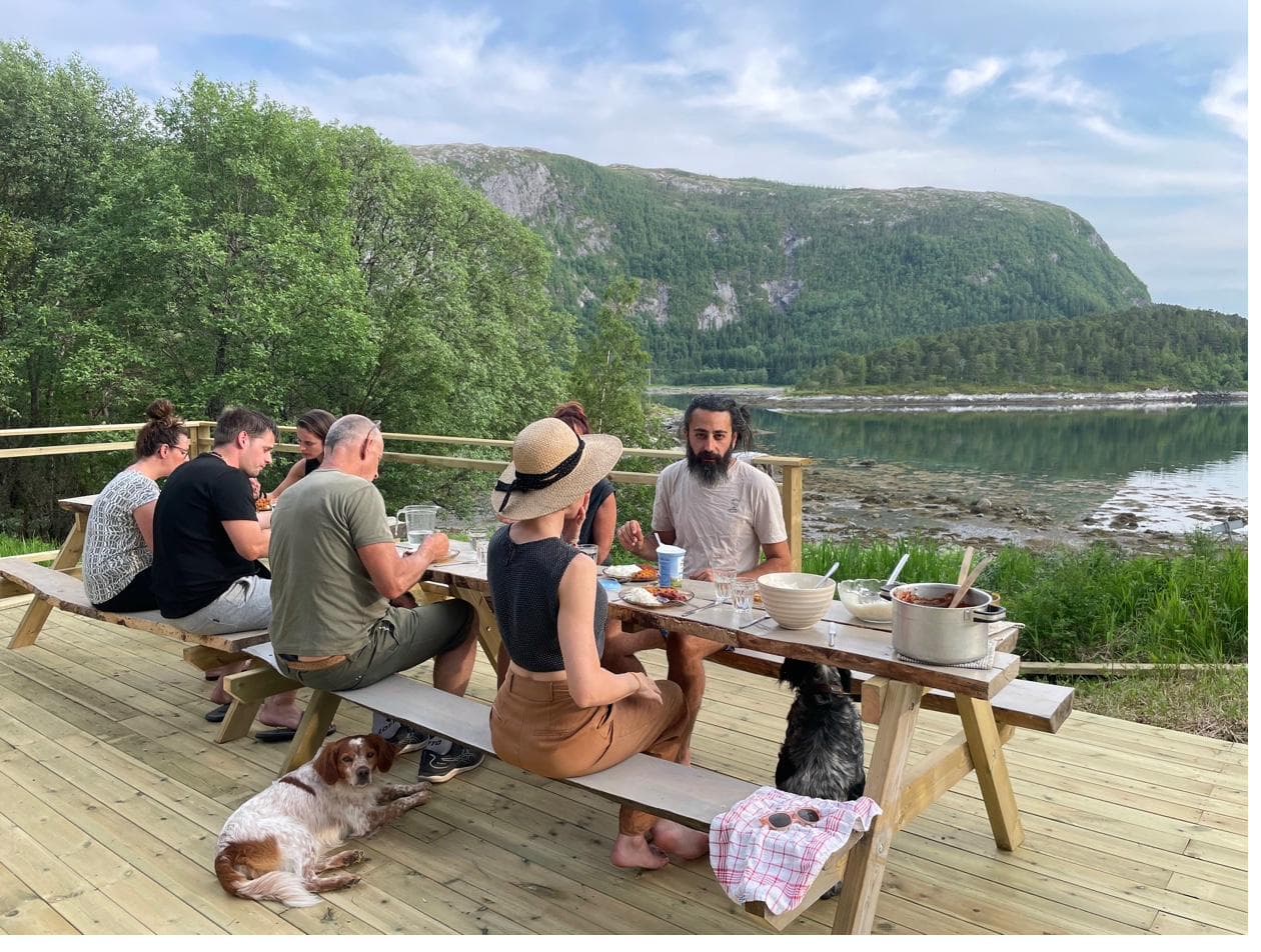 Gruppe mennesker som spiser ved langbord ved fjorden