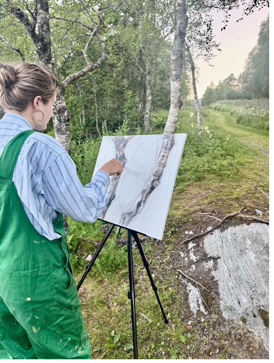 Kunstner som maler ved staffeli blant bjørketrær